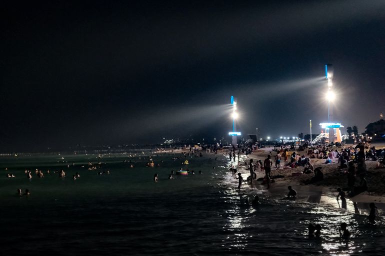Floodlights illuminate the Umm Suqeim beach in Dubai as people cool off in at night on May 23, 2025. United Arab Emirates registered a sizzling 50.4 degrees Celsius on May 23, the highest on record for May, following weeks of sweltering temperatures in the desert nation acutely vulnerable to climate change. (Photo by Giuseppe CACACE / AFP)