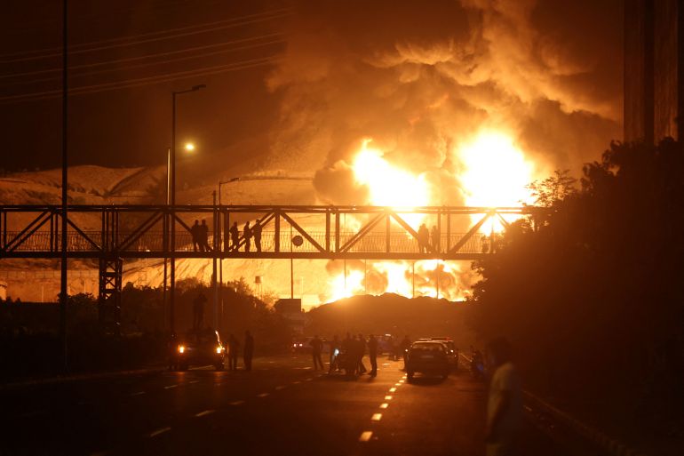 People watch from a bridge as flames from an Israeli attack rise from Sharan Oil depot, following Israeli strikes on Iran, in Tehran, Iran, June 15, 2025. Majid Asgaripour/WANA (West Asia News Agency) via REUTERS ATTENTION EDITORS - THIS PICTURE WAS PROVIDED BY A THIRD PARTY