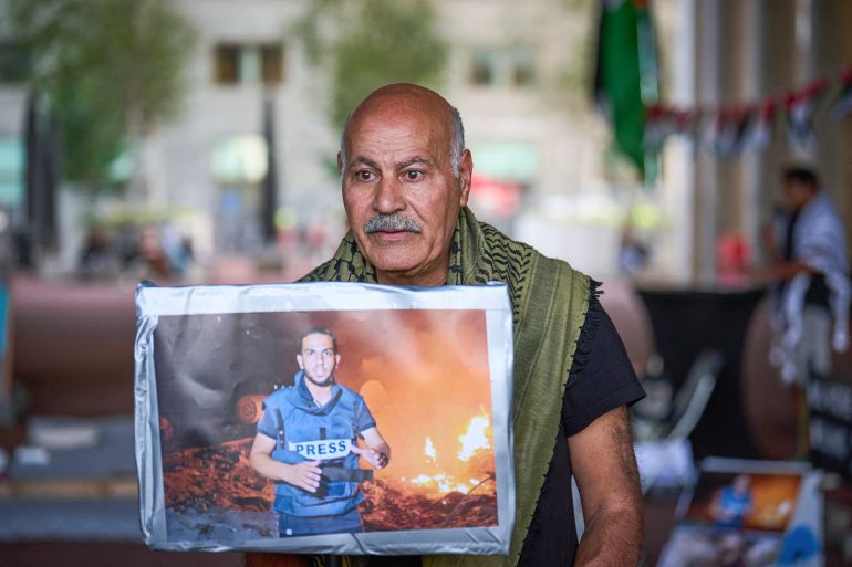 A man holds a portrait of the late Palestinian journalist Anas Al-Sharif as he gathers for a vigil to commemorate all journalists killed in Gaza, at the Ministry of Foreign Affairs in The Hague, on August 11, 2025. (Photo by Phil Nijhuis / ANP / AFP) / NETHERLANDS OUT