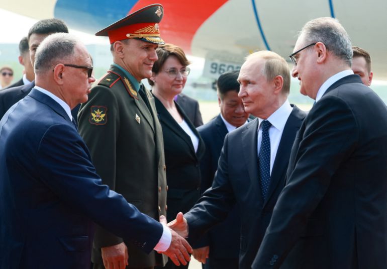 In this pool photograph distributed by the Russian state agency Sputnik, Russia's President Vladimir Putin shakes hands with Russian Trade Representative to China Alexey Dakhnovsky (L) alongside Russian Ambassador to China Igor Morgulov (R) upon his arrival at the airport in Tianjin on August 31, 2025.