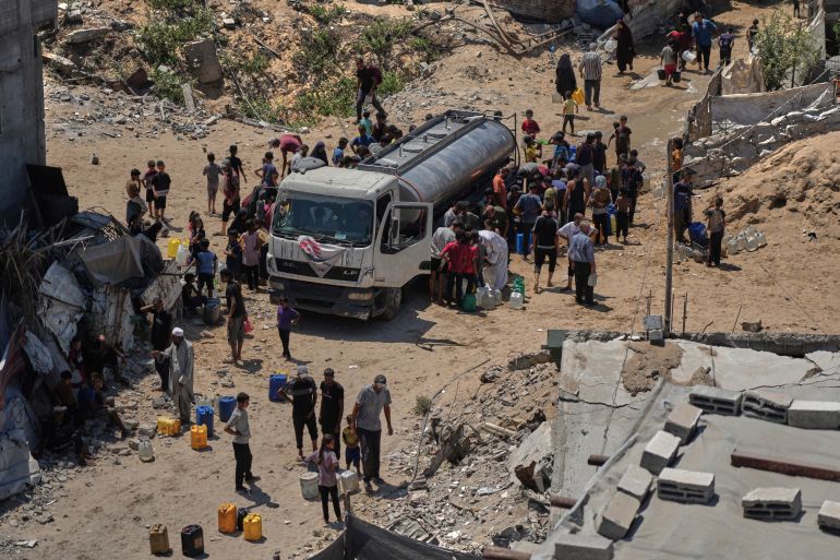 Displaced Palestinians gather to collect water from a truck in Gaza City, Saturday, Aug. 23, 2025. (AP Photo/Jehad Alshrafi)